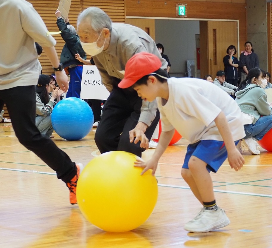 黄色いボールを小学部6年生とお客さんが遺書に転がしています。