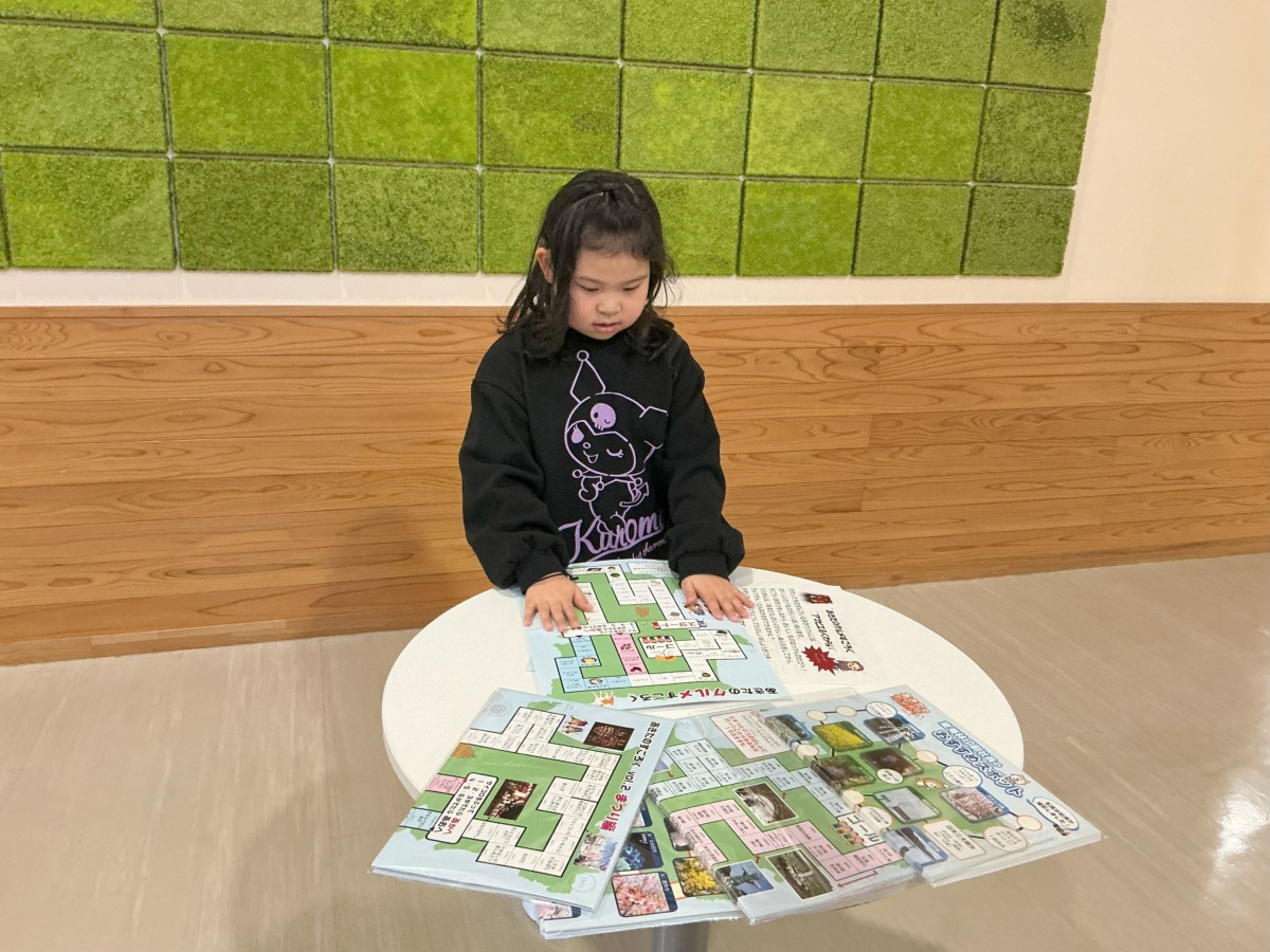 小学生が机の上にひろげたあきたのすごろくを見ている写真