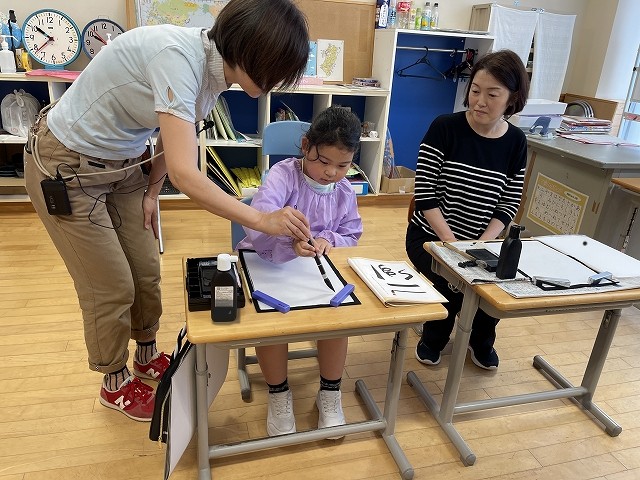 先生に手を添えてもらいながら書いている写真