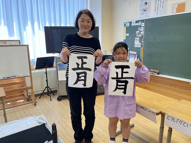 完成した習字を持ち先生と並んで立っている写真