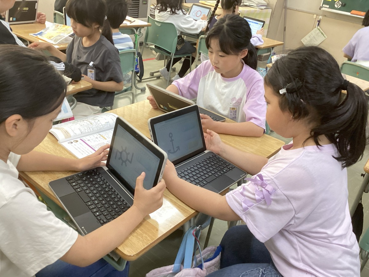 社会科の授業で友達に誘われて一緒にタブレットを使用しながら地図記号クイズに挑戦している写真