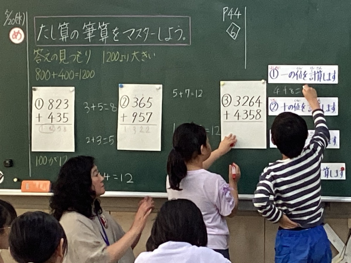 算数の授業で黒板の前に立って筆算している写真