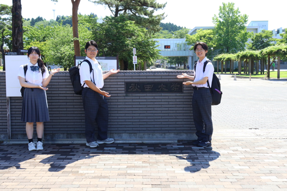 秋田大学の正門の前で高等部生徒3名が集合写真を撮りました。