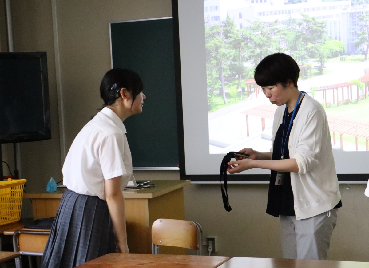 大学概要説明が始まる前に、説明を担当してくださる職員に音声補聴システムのロジャーマイクを生徒が手渡しています。