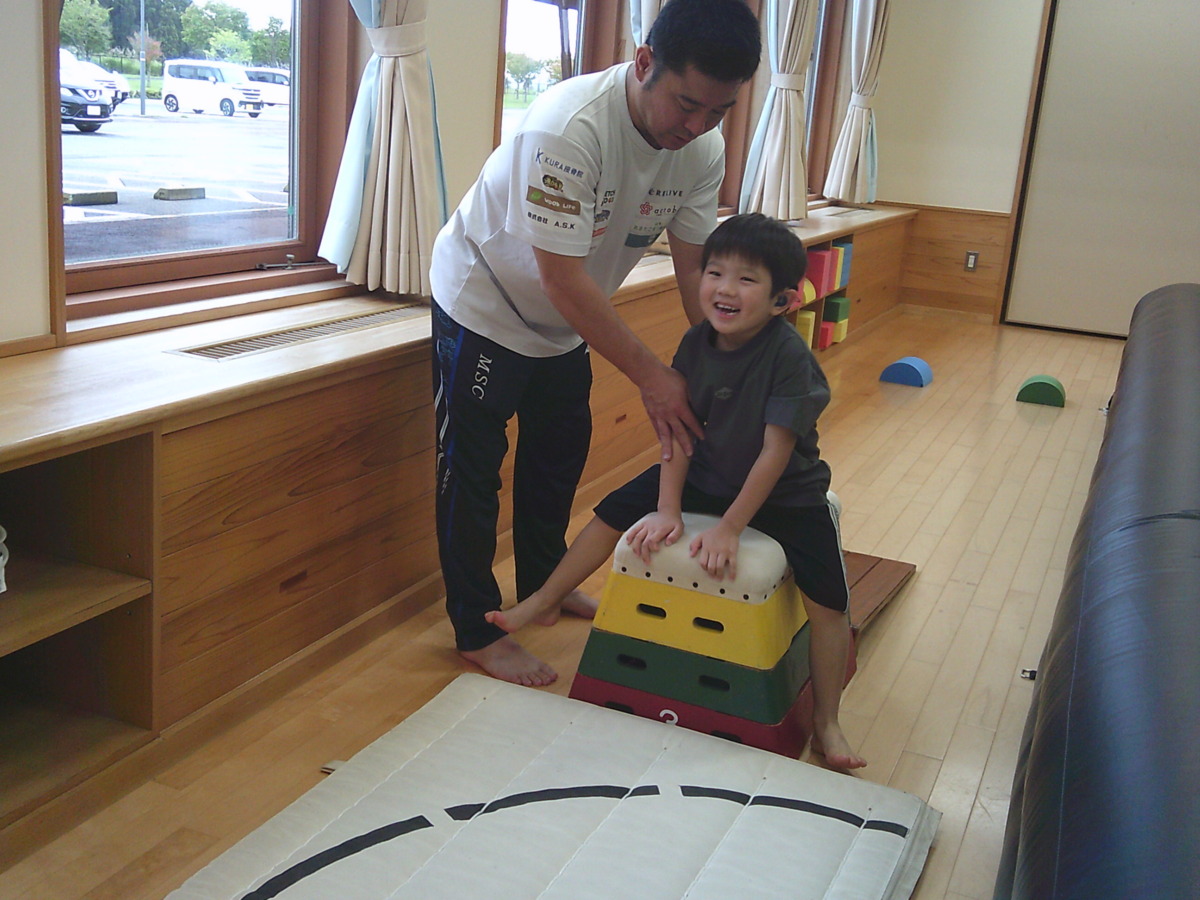 松村先生に補助してもらいながら、男の子が笑顔で跳び箱にまたがっている写真