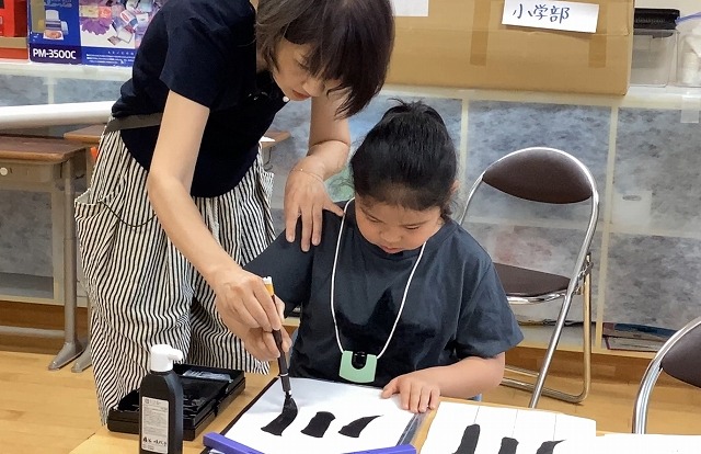 女の子が筆の動かし方を教わっている写真