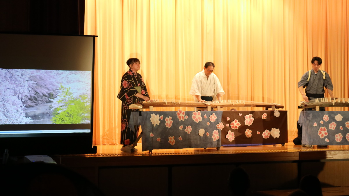ステージ上で、テーブルに乗った琴を、着物を着て演奏している生徒3名