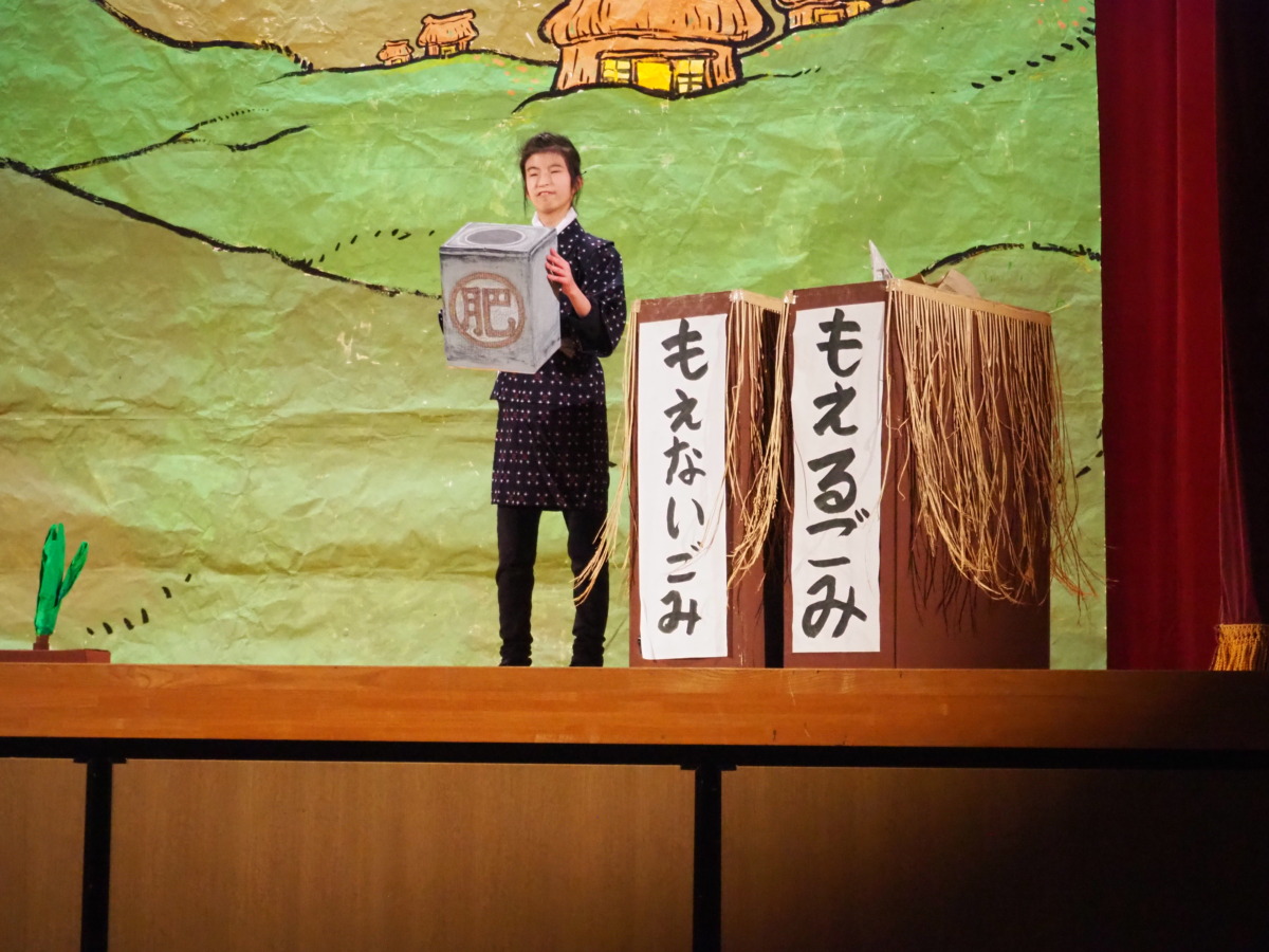 「もえるごみ」「もえないごみ」と書かれたごみ箱の前で、缶のごみを掲げる村人役の生徒