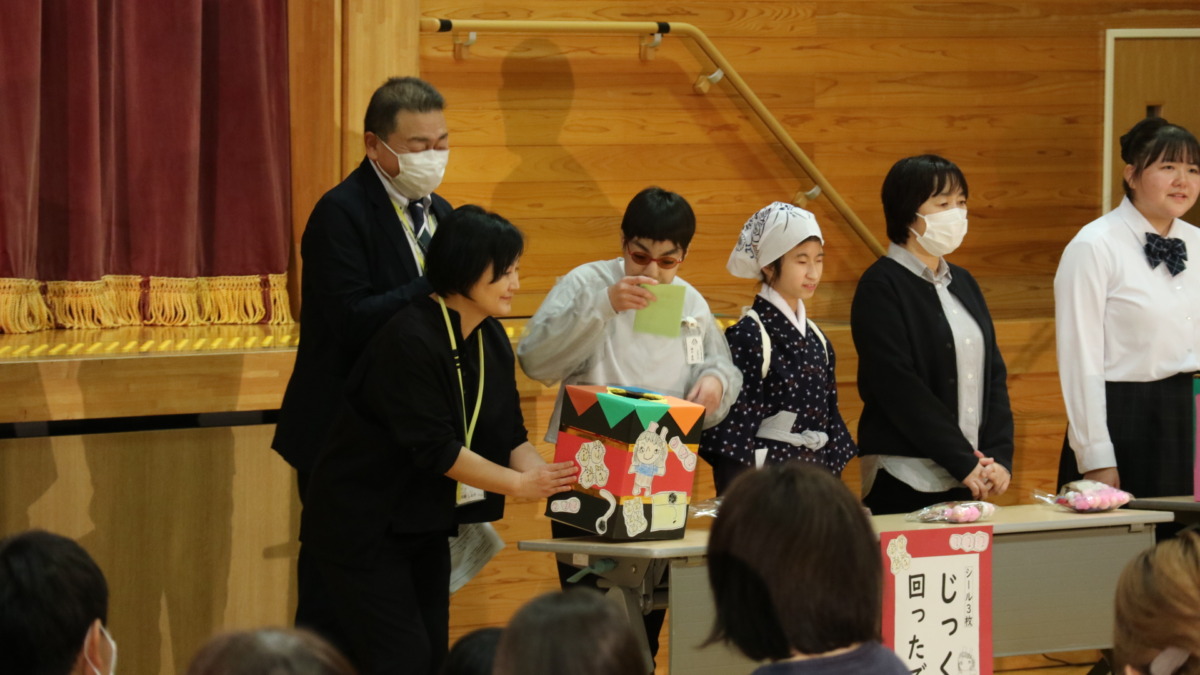 実行委員の児童生徒数名が、ステージの前で抽選箱を順番に引いている様子