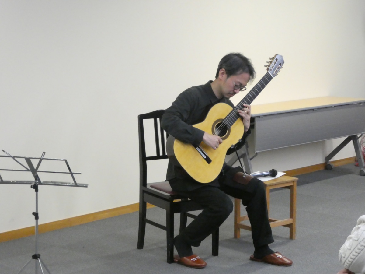 椅子に座り、クラシックギターを抱えるように演奏する村治奏一さん