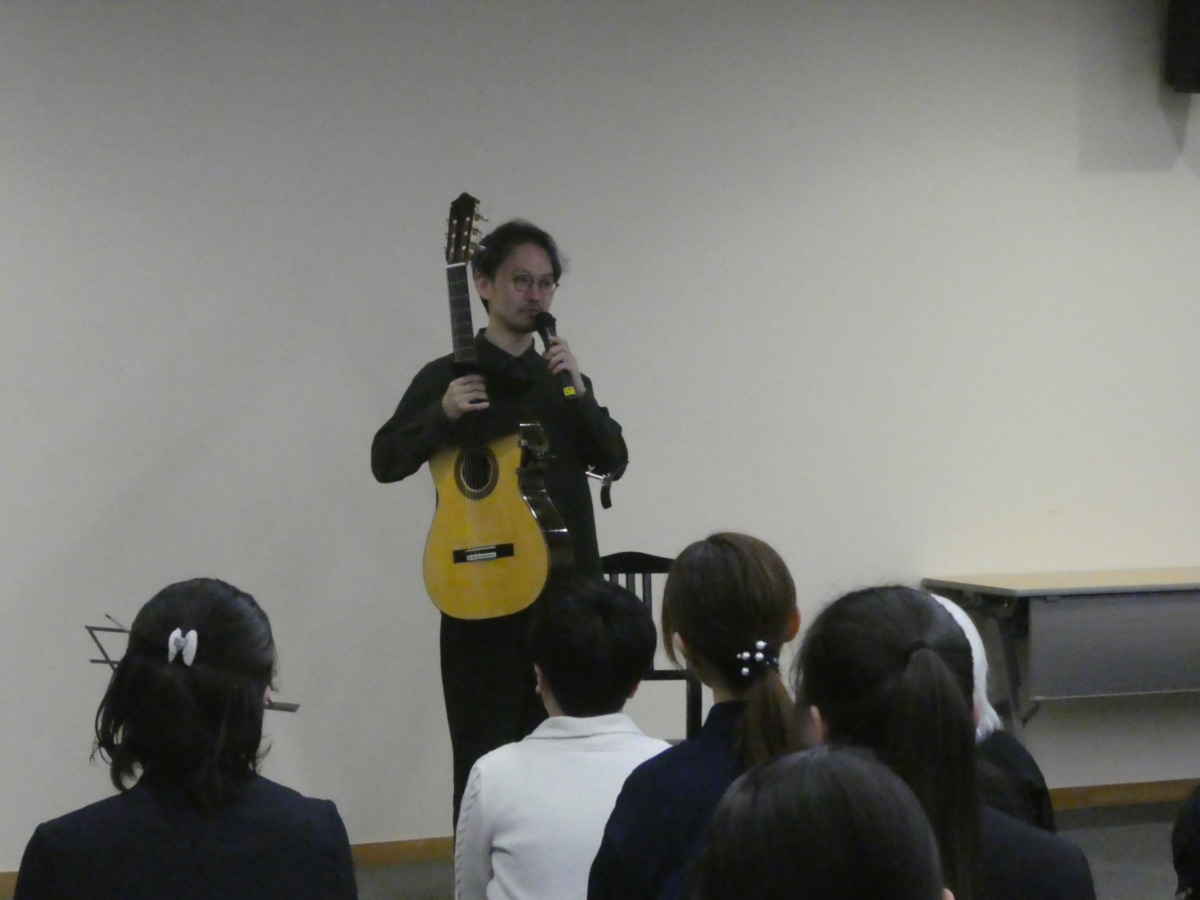 右手にクラシックギター、左手にマイクを持ち、立って鑑賞者に語りかける村治奏一さん