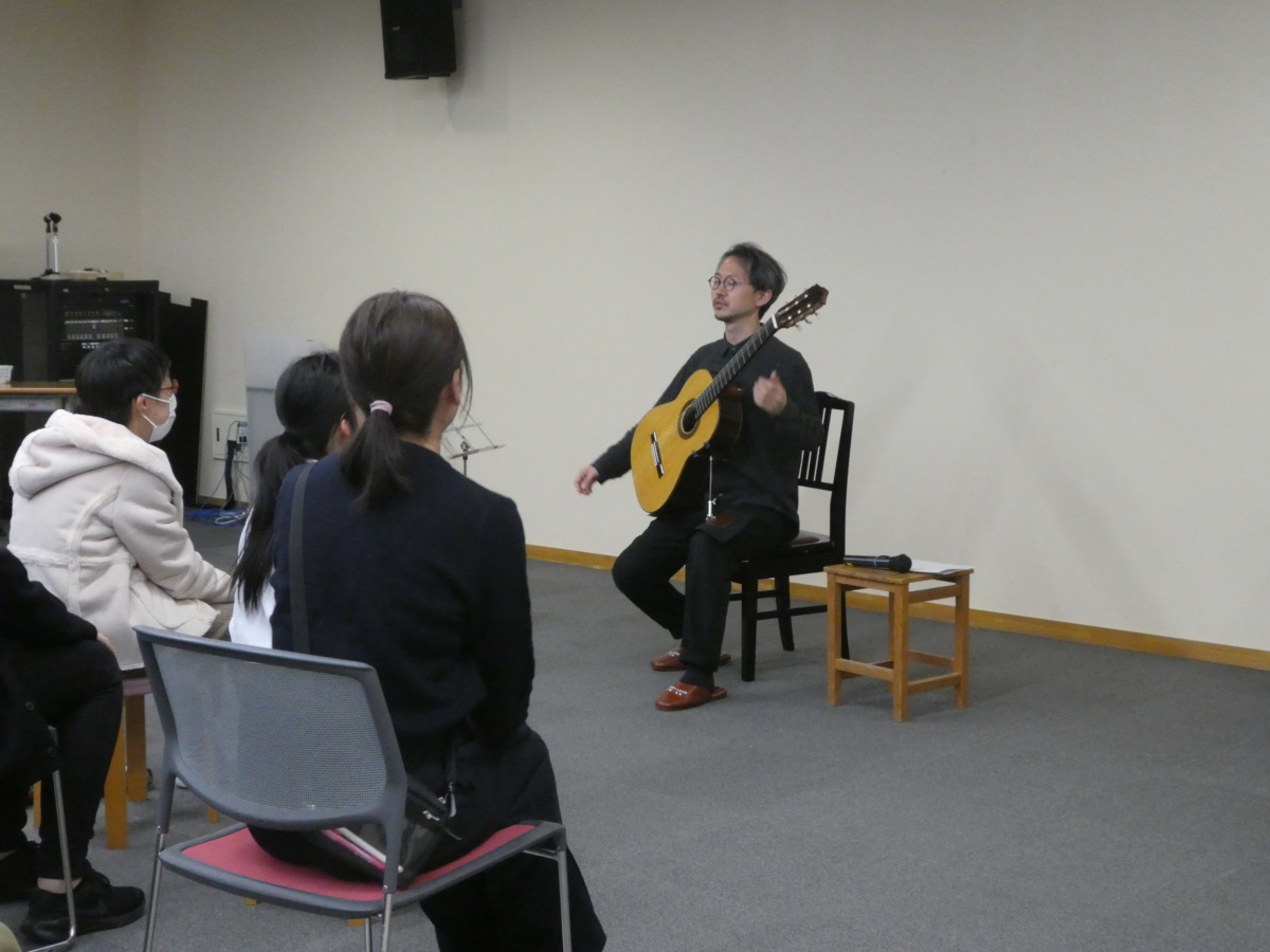 椅子に座って演奏している村治奏一さんと見入っている鑑賞者たち