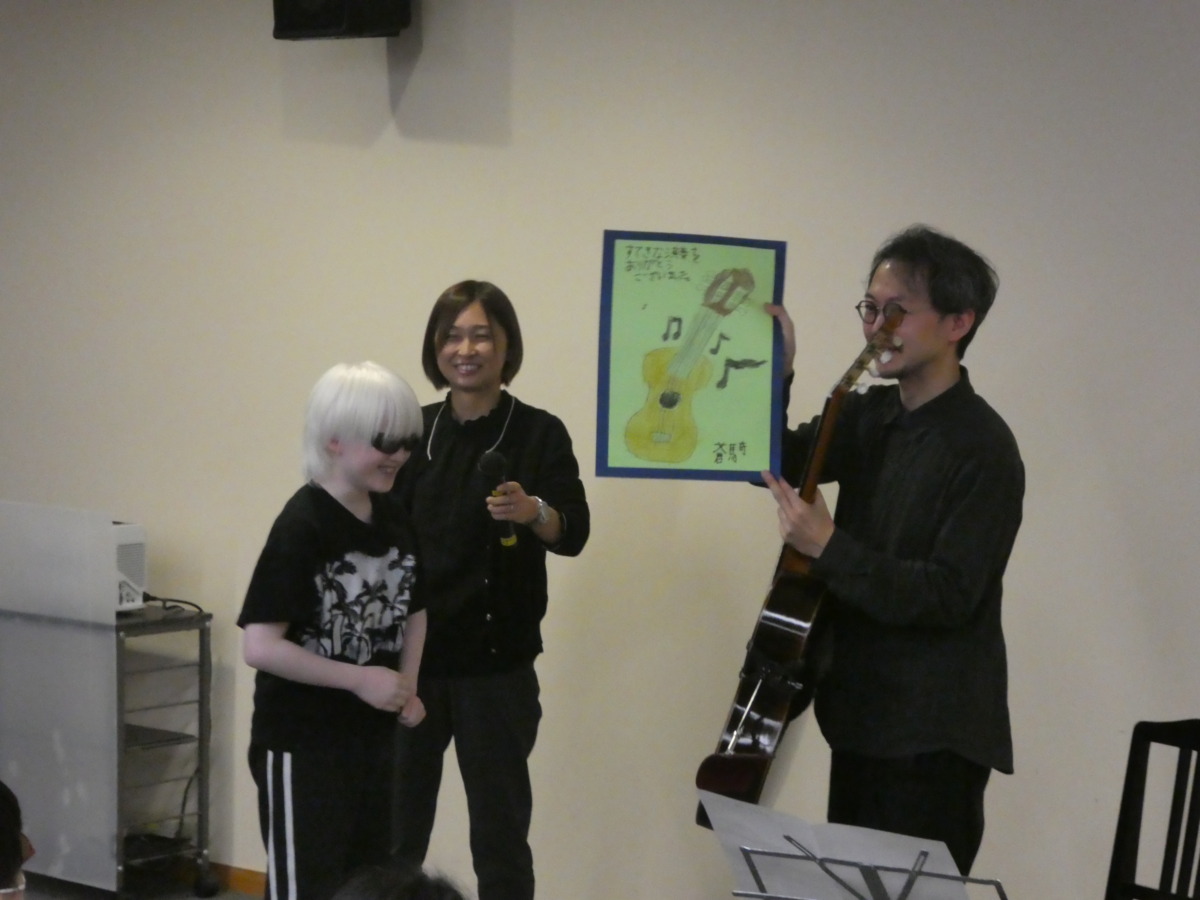 本校児童から村治奏一さんへ、ギターのイラストをプレゼントしている様子