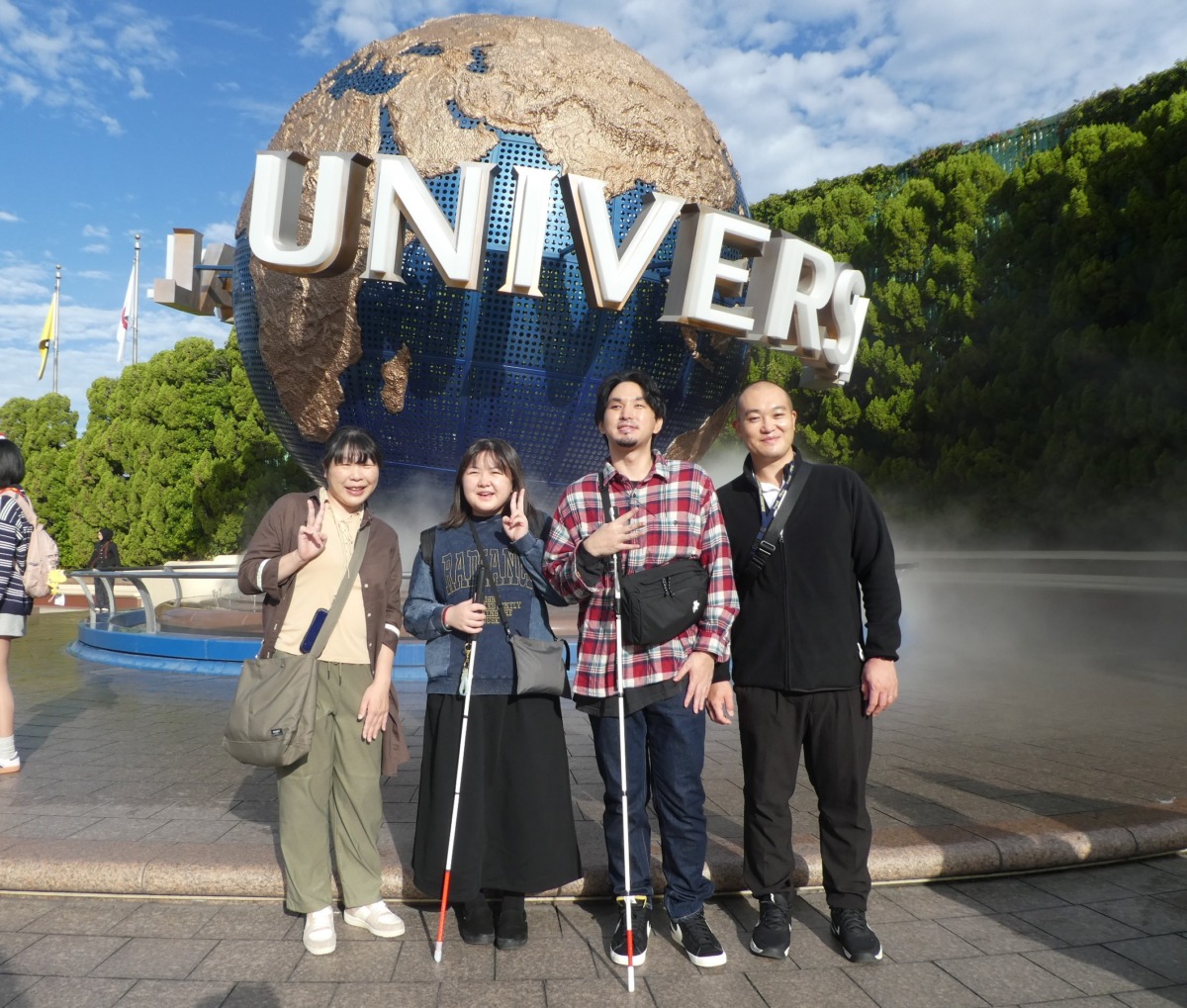 直径10メートルほどの地球儀のモニュメントの前で、生徒二名と教員二名が、生徒二名を間に挟む形で並んでいる様子