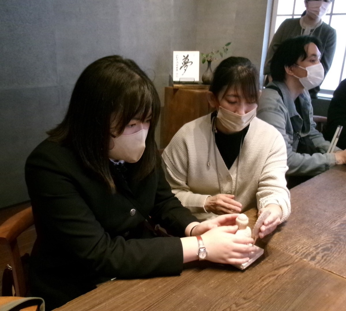 生徒と教員が座り、テーブル上にある手のひらサイズの模型を一緒に触っている様子