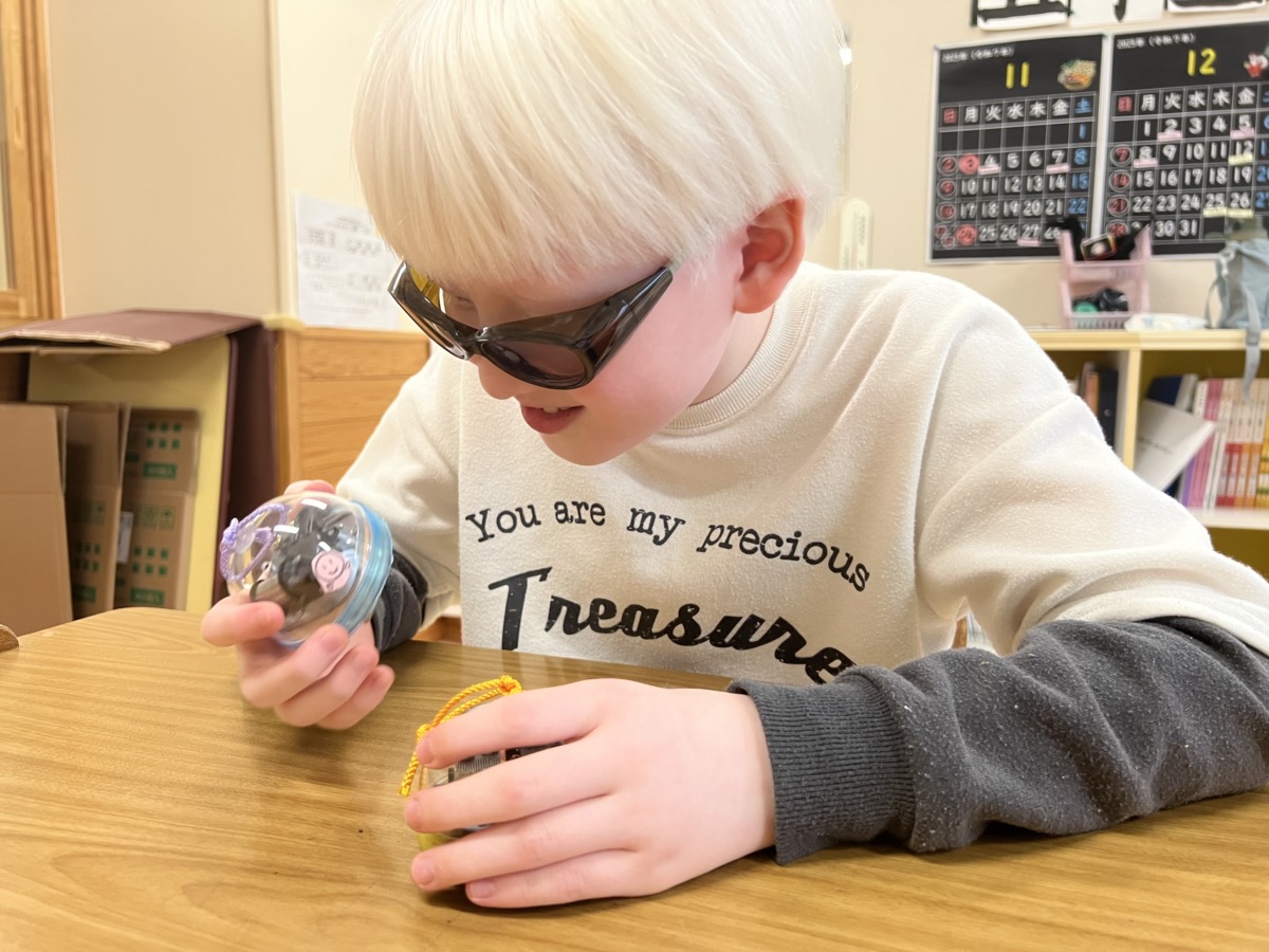 椅子に座り、机の上で両手に持ったオルゴールを眺めている児童