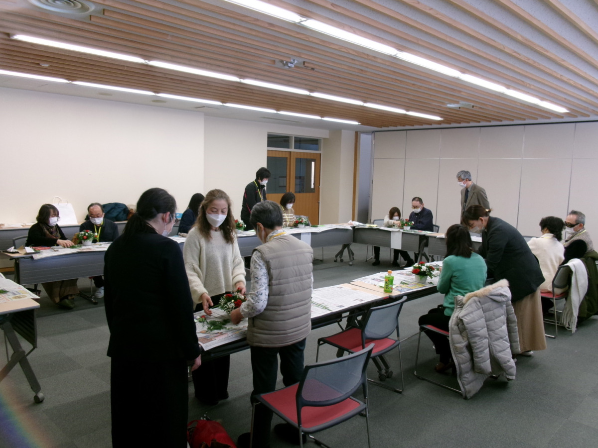 広い部屋に長テーブルが長方形に並べられており、数組に分かれて活動している様子