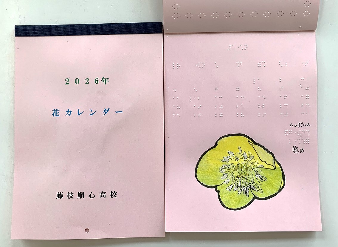 ピンク色の背景にハンコのような青文字で「花カレンダー」と書かれた表紙。開くと点字でカレンダーが記載されており、ページの下部に「ヘレボルス」の花の絵と名前が点字で記載されている。