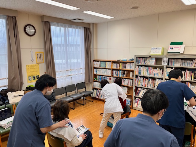 椅子に座った4名の患者に、生徒・職員がそれぞれ施術を行っている様子