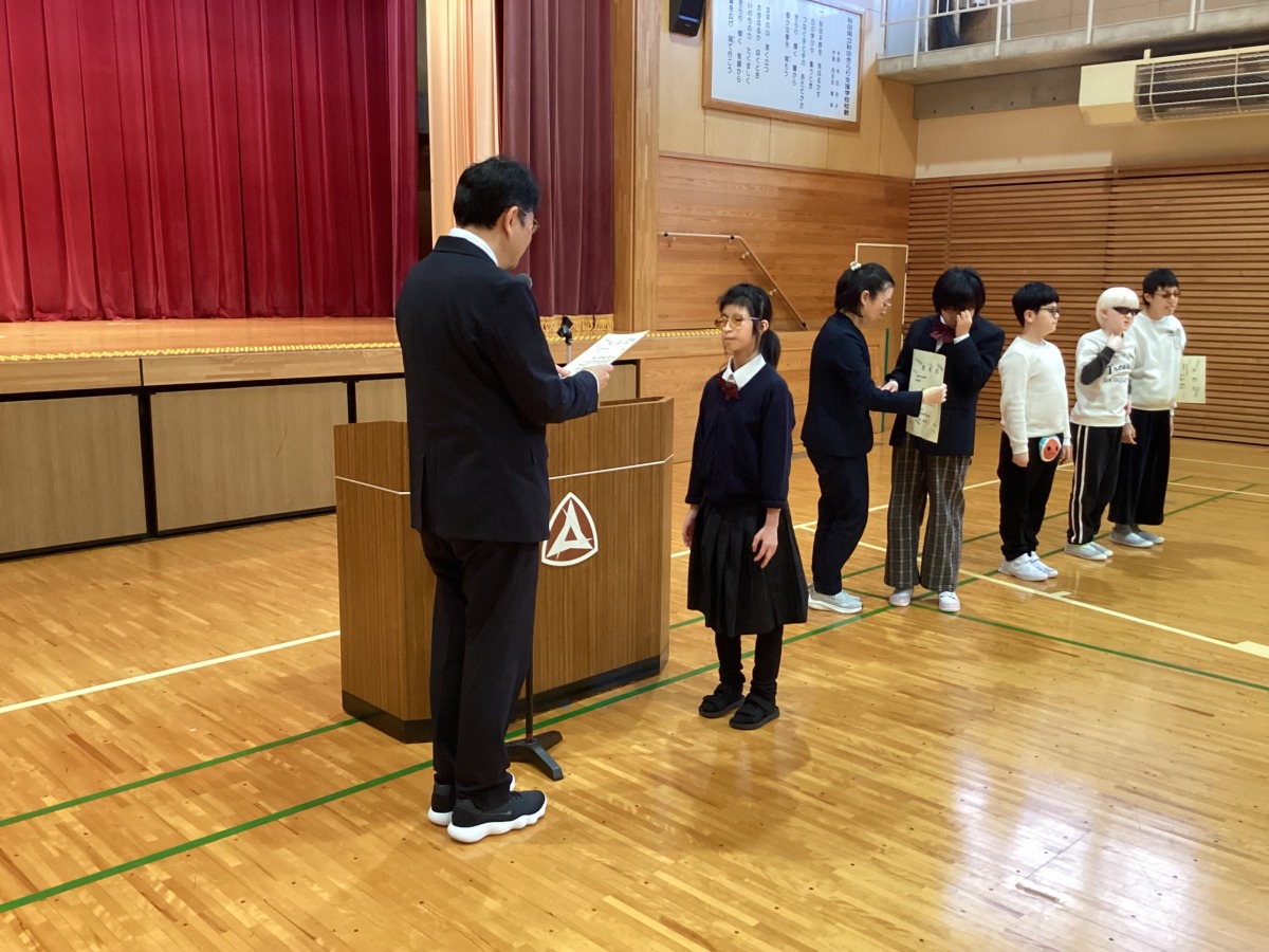 演台の前で校長先生が読み上げた賞状を受け取っている中学部生徒の様子