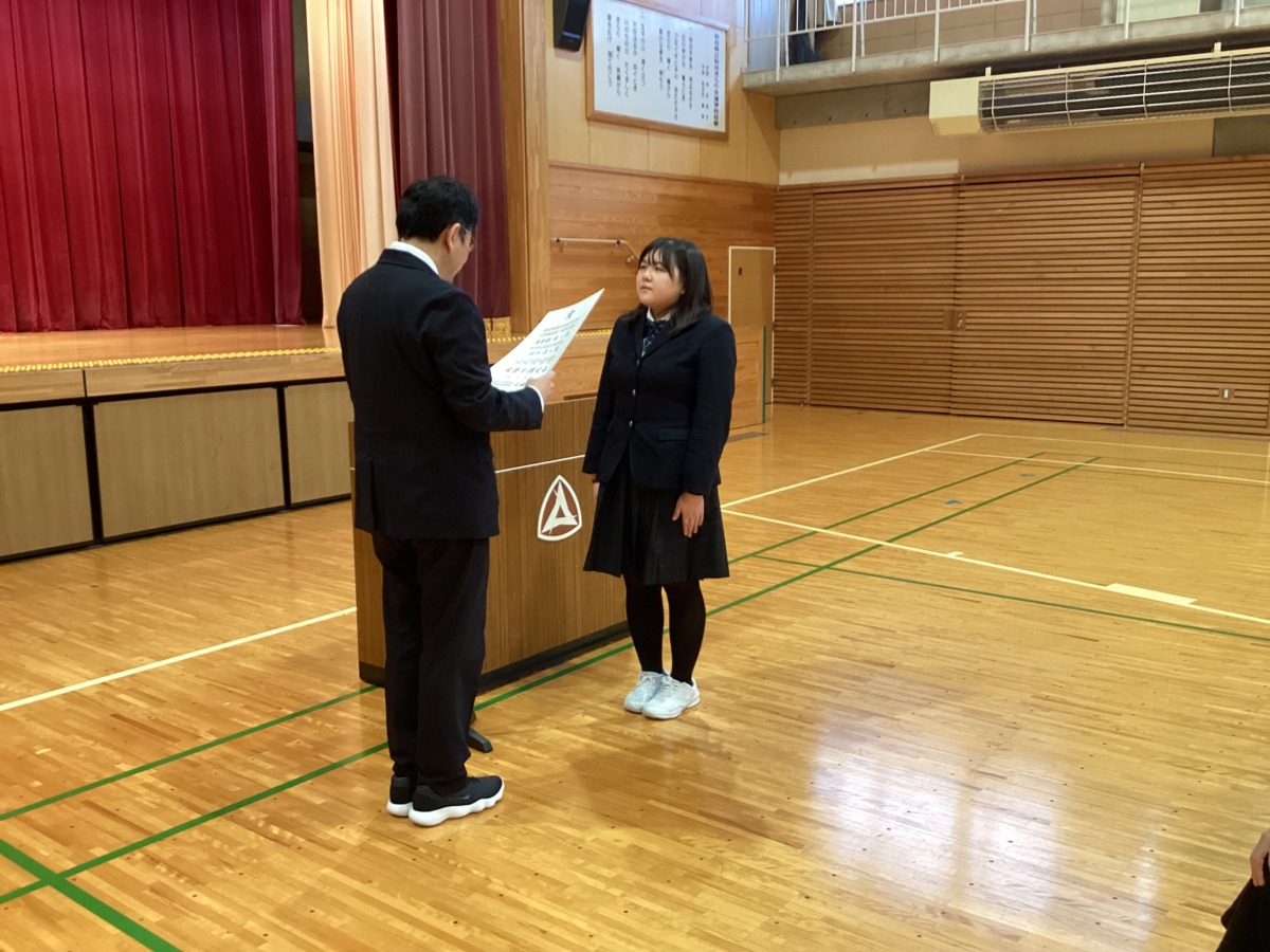 演台の前で校長先生が読み上げた賞状を受け取っている高等部生徒の様子