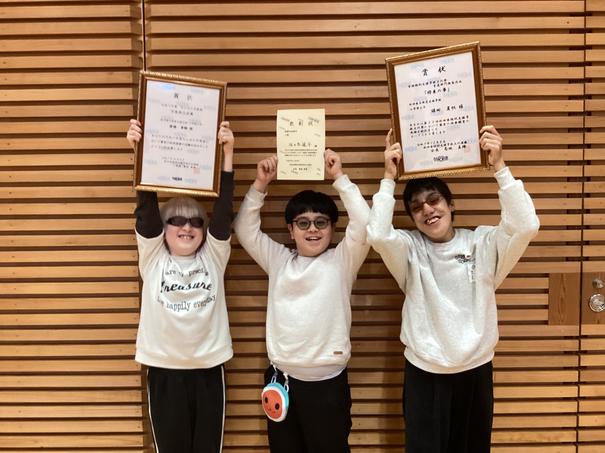 小学部児童３名が、各自受け取った賞状を両手で頭の上に掲げている様子