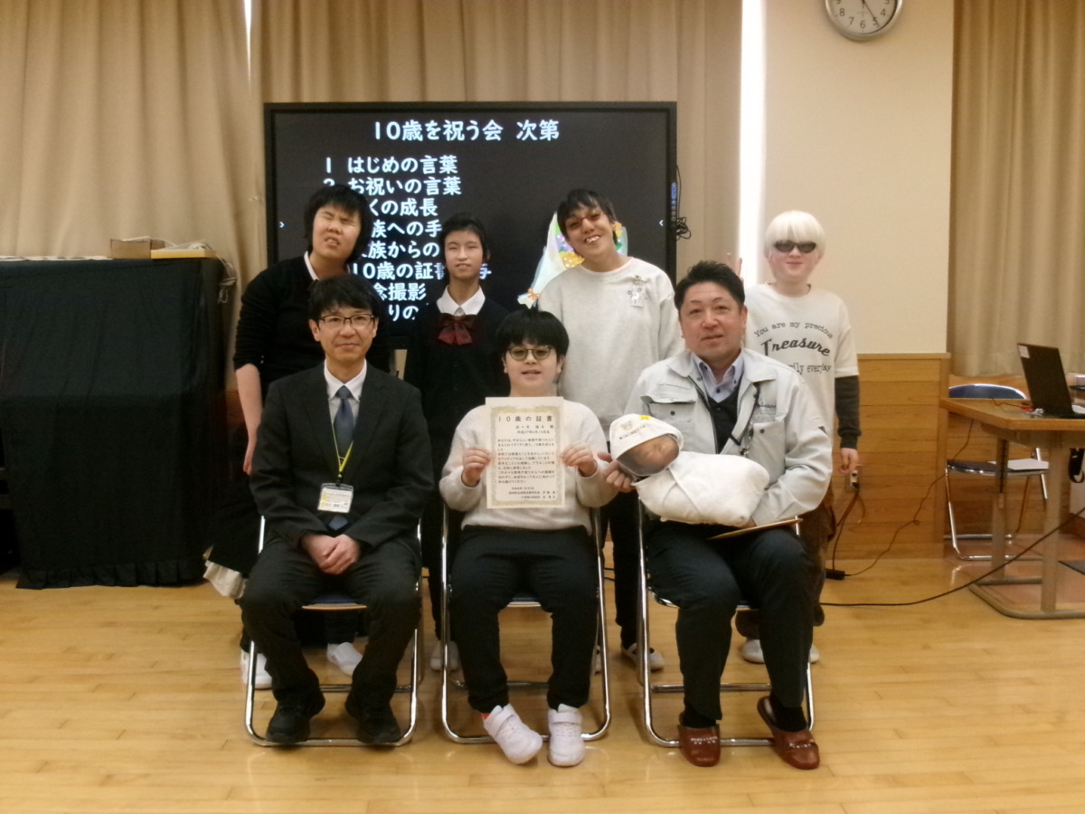 前列に10歳を迎えた児童1名、父親、教頭が椅子に座って並び、後列に小・中学部の児童生徒4名が並んで立っている記念写真