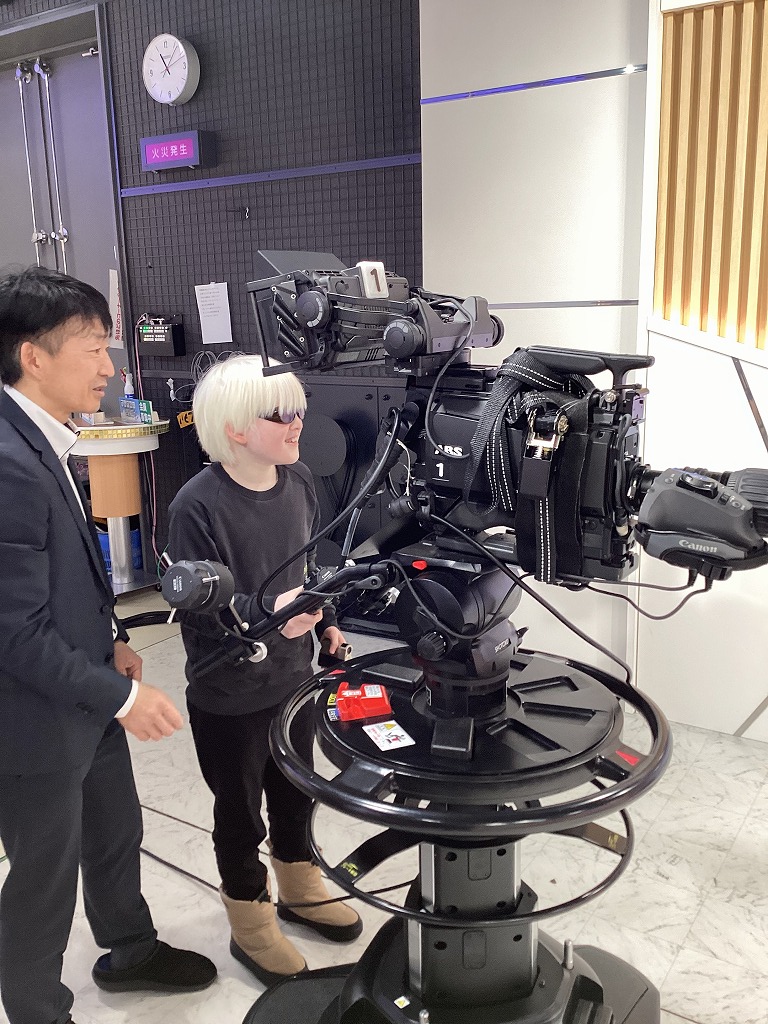 児童が自分より少し背の高い撮影用カメラの手前のバーをつかんで動かしている様子