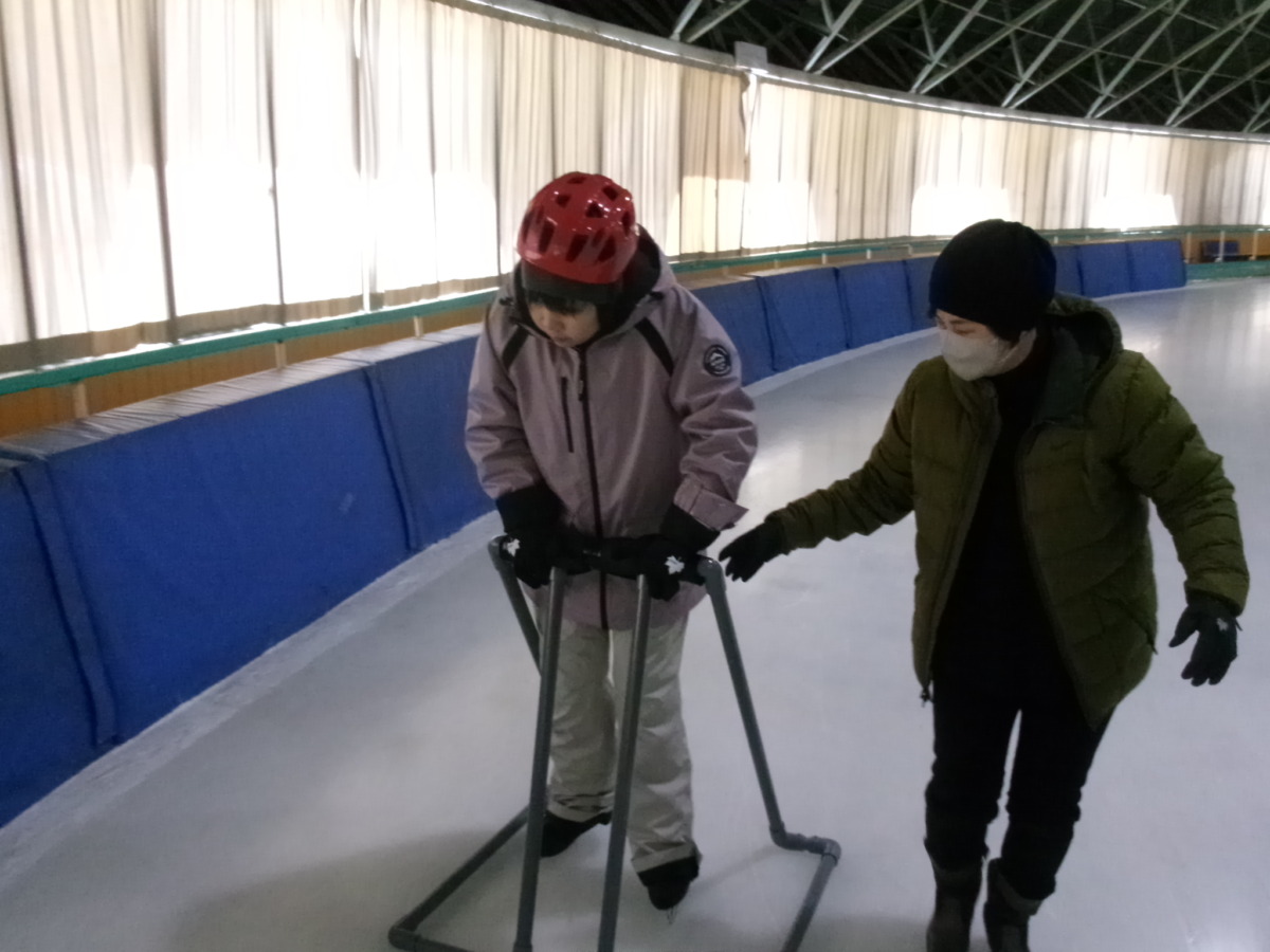 生徒1名が、補助具や職員の補助を受けながらリンクを進行方向通りに歩行している様子