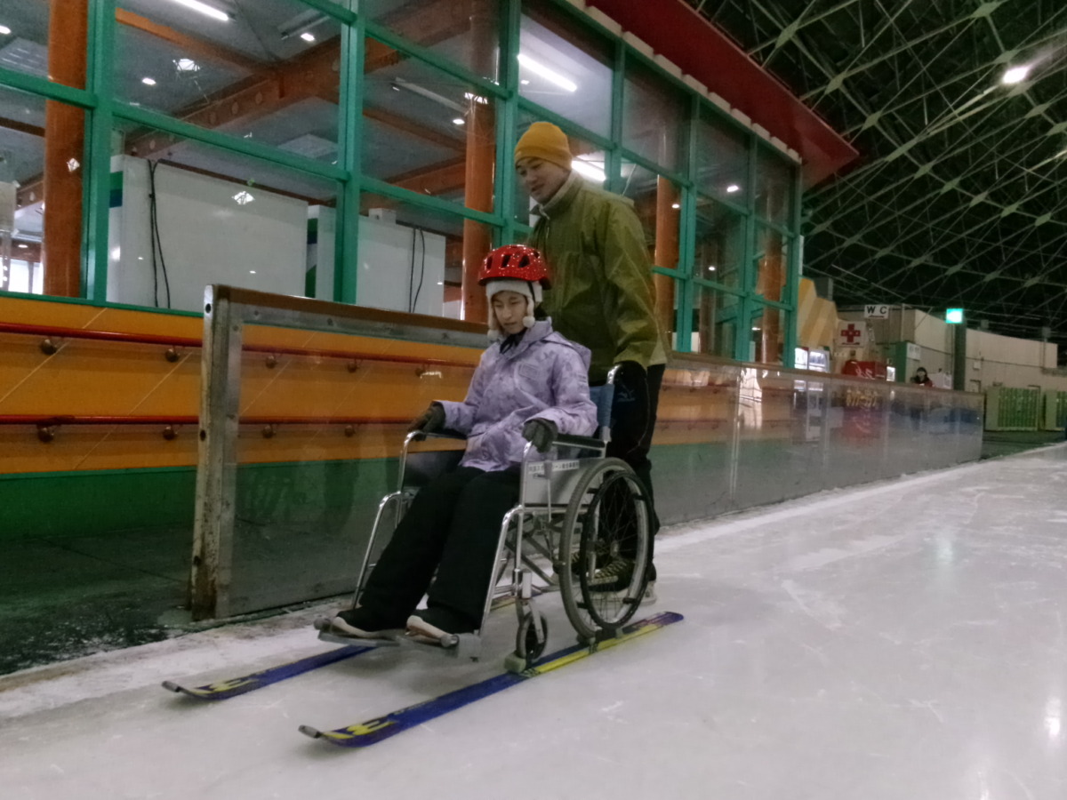 生徒が、両輪にスキー板がついた車いすに乗って、職員に押してもらっている様子