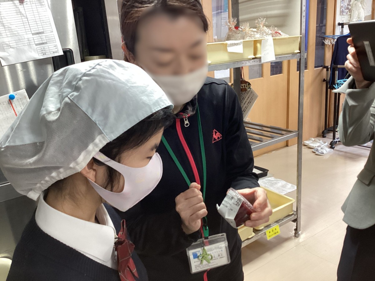 カップに入ったスイーツの商品ラベルを確認しながら、説明を受けている生徒の様子