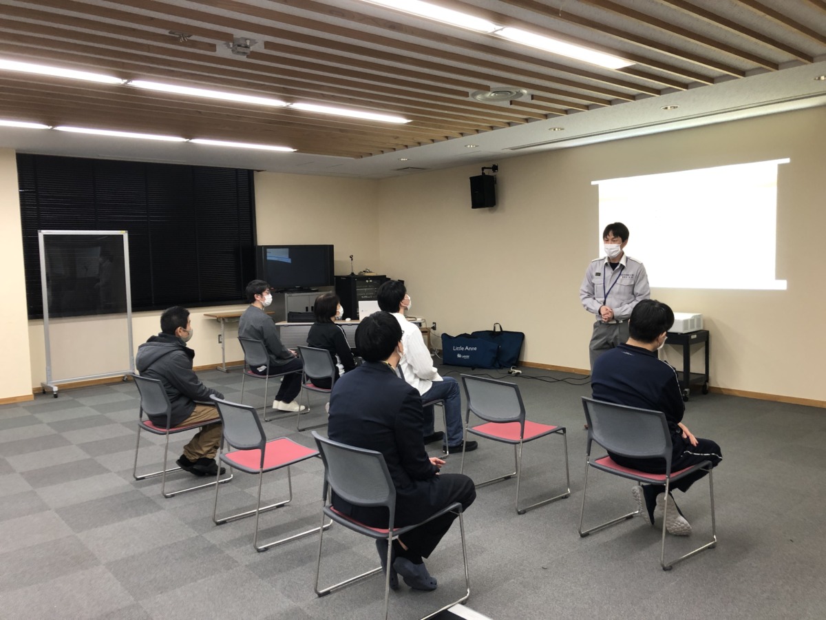 壁に映されたスライドの前に講師の方が立ち、その手前に生徒・職員が座って話を聞いている様子。