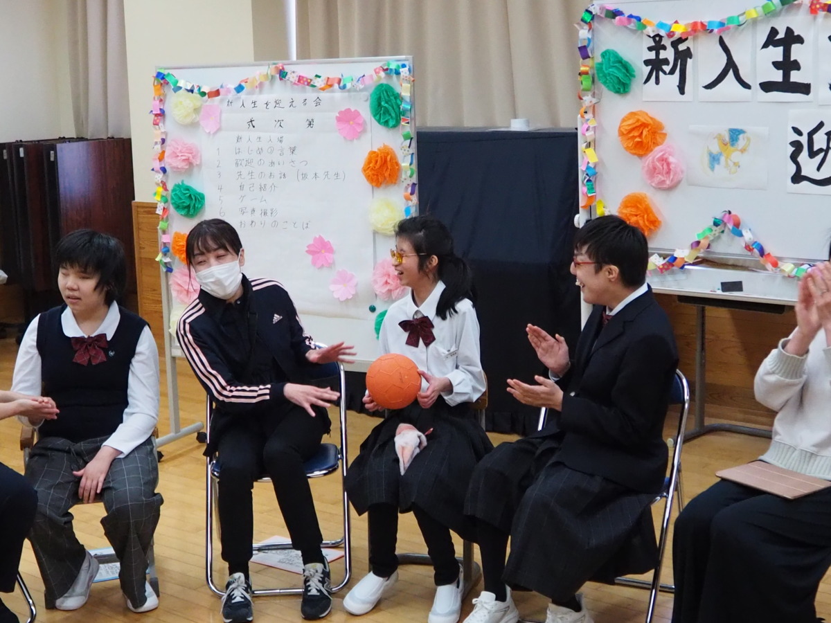 輪になって座った児童生徒職員が、「爆弾」に見立てたオレンジ色のボールを受け渡しあっている様子