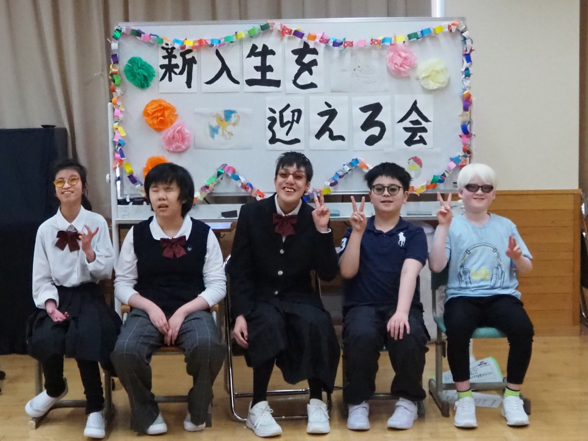 「新入生を迎える会」と装飾されたホワイトボードの前で、新雄性を中心に児童生徒５人が並んで座っている様子