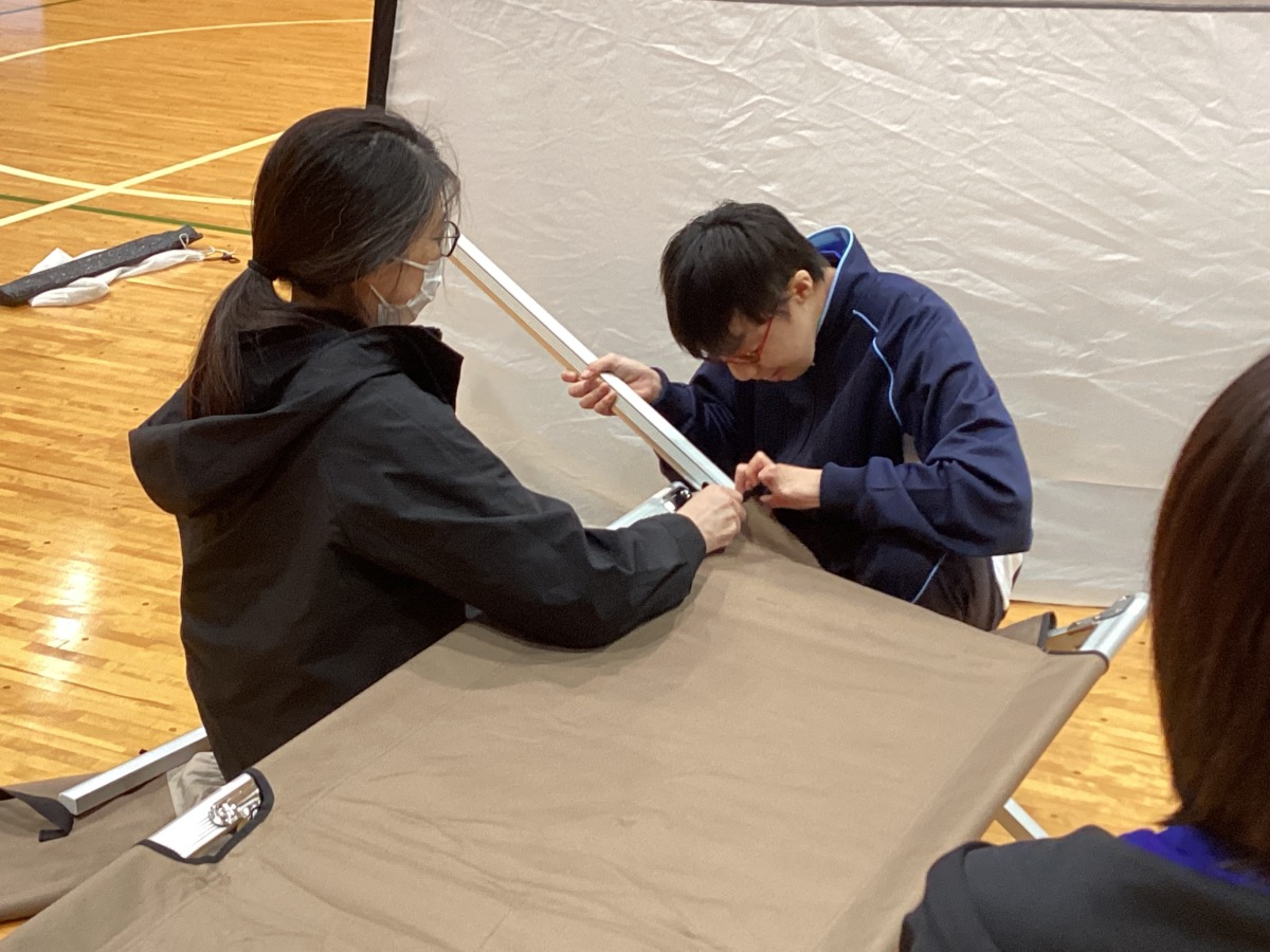折り畳み式簡易ベッドのパーツの接合部を、保護者と確認しながら組み立てている様子。