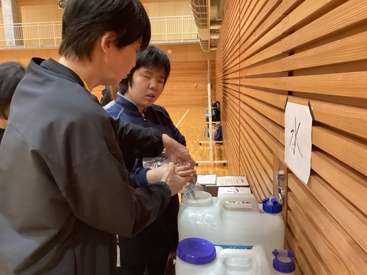 生徒がタンクの補給口を触って確認しながら、ペットボトルの水を移している様子。
