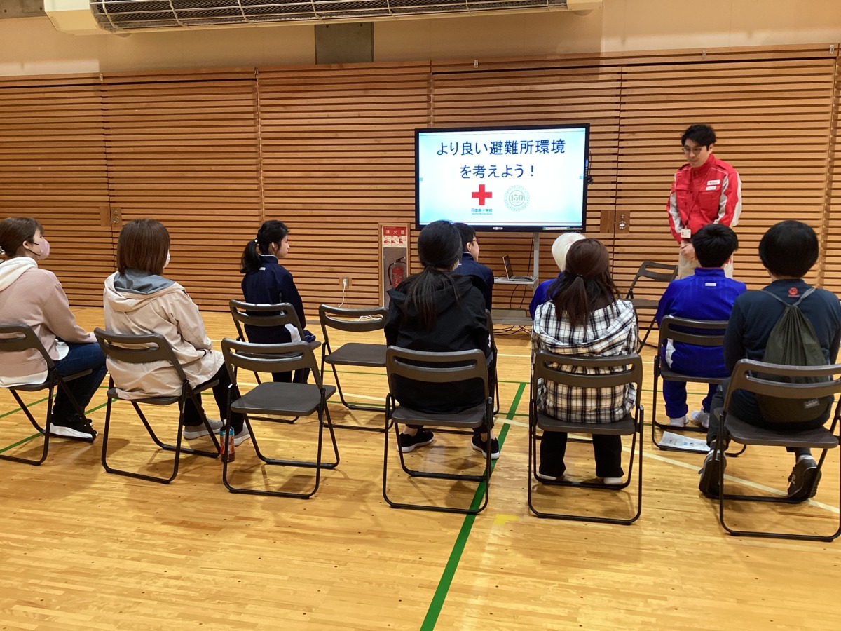 スライドを写した電子黒板の横で話す講師の先生と、電子黒板の前に並んで座っている児童生徒と保護者