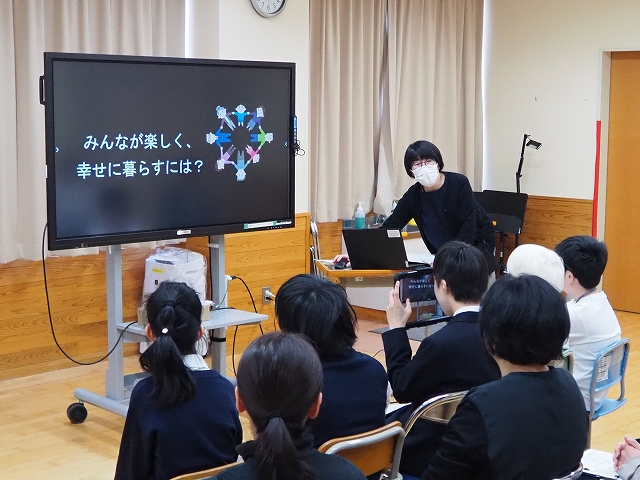 電子黒板の前に児童生徒が座り、職員がスライドを使いながら説明をしている様子。