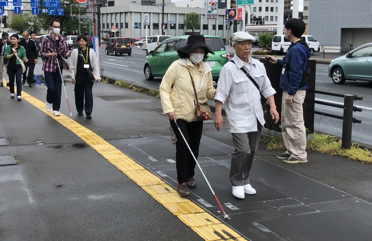 参加者が白杖を持ち、別の参加者の手引きを受けながら点字ブロックの上を歩行している様子