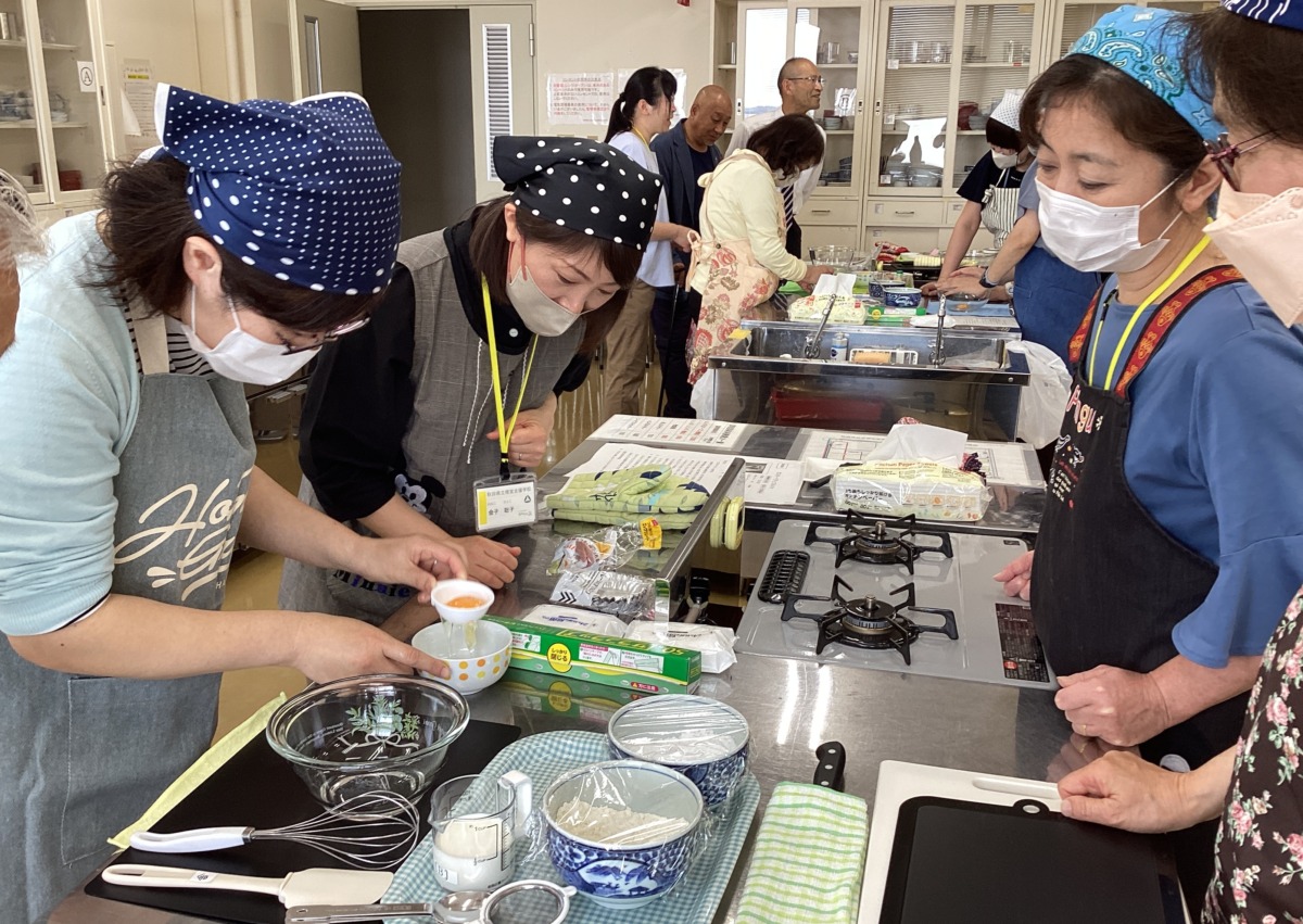 参加者が卵黄と卵白を分ける調理器具を、職員が付き添いながら使っている様子。