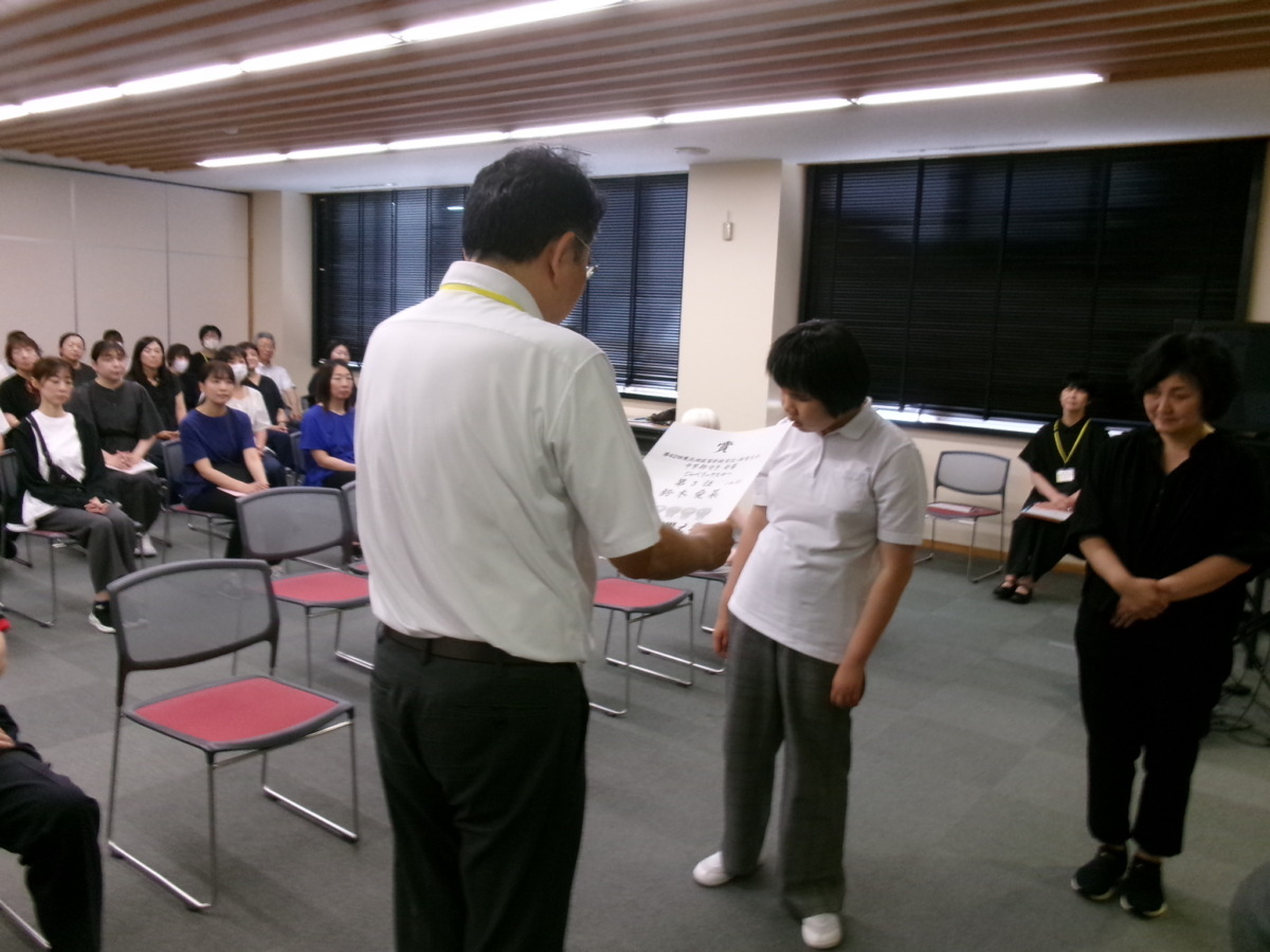 職員や児童生徒が見守る前で、校長先生から中学部生徒1名に対して賞状を読み上げている様子。