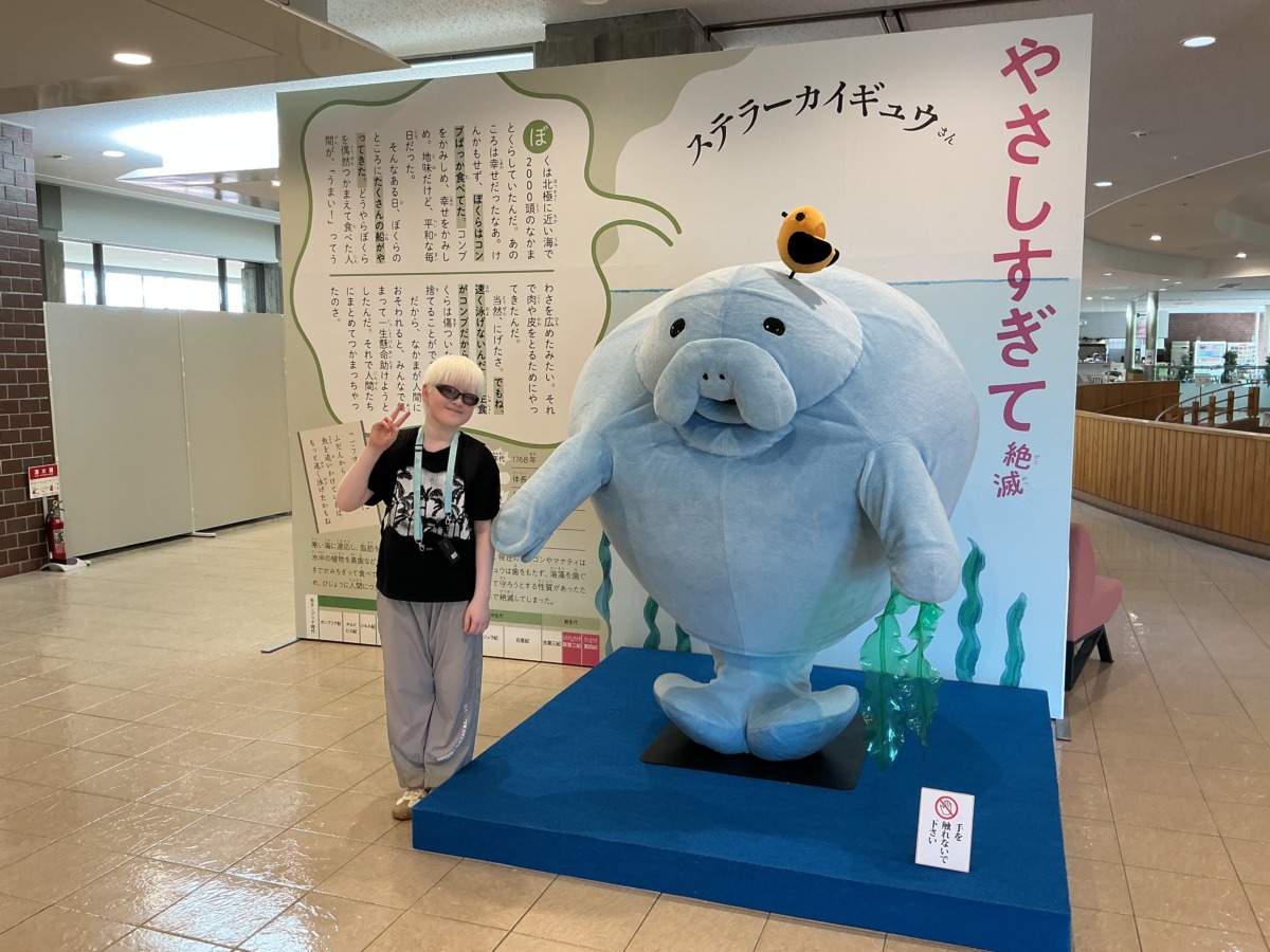 自分よりも一回り大きい「ステラーカイギュウ」というアザラシのような生き物のぬいぐるみと写真を撮る児童