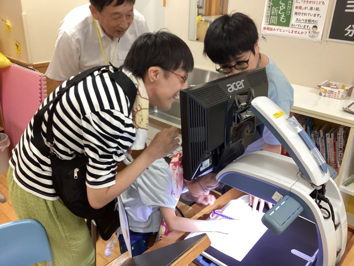 児童生徒三名が、拡大読書器のモニターをのぞき込んで確認しながら活動している様子。