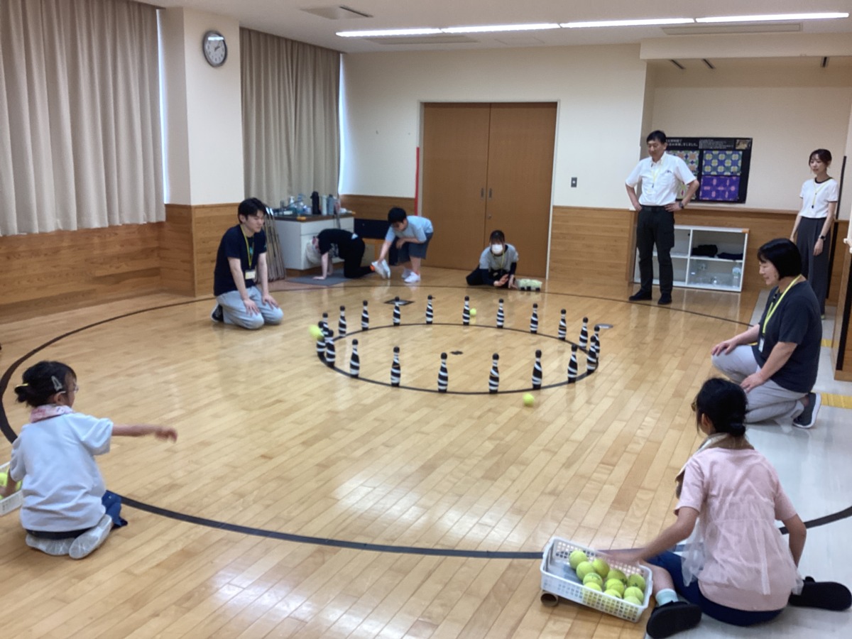 中心から直径2メートルの円に等間隔で並べられたピンに対し、中心から直径6メートルの位置からテニスボールを投げている児童生徒と職員