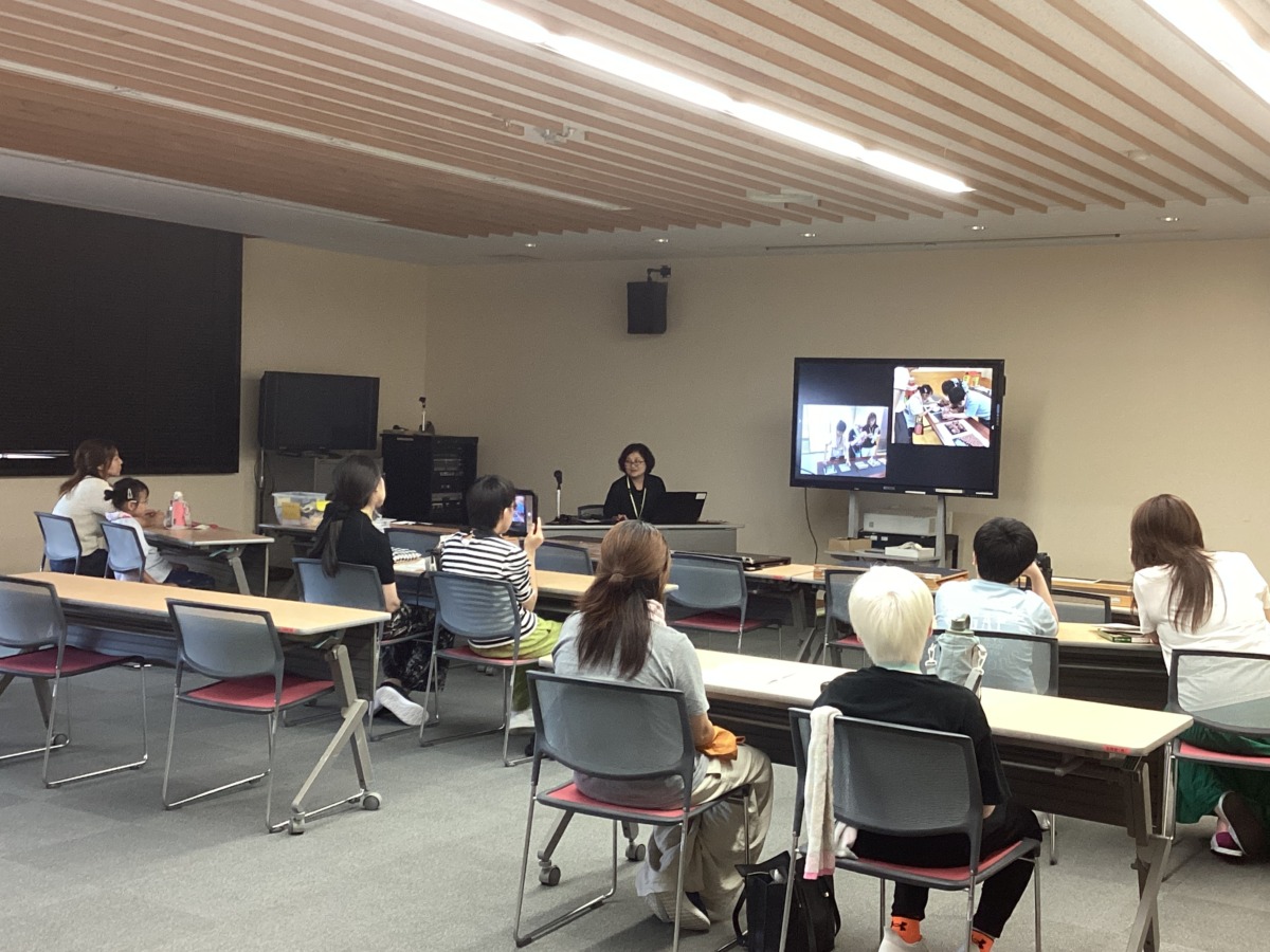 家庭ごとにテーブルに座り、前方のモニターに写された活動の写真のスライドを見ている様子。