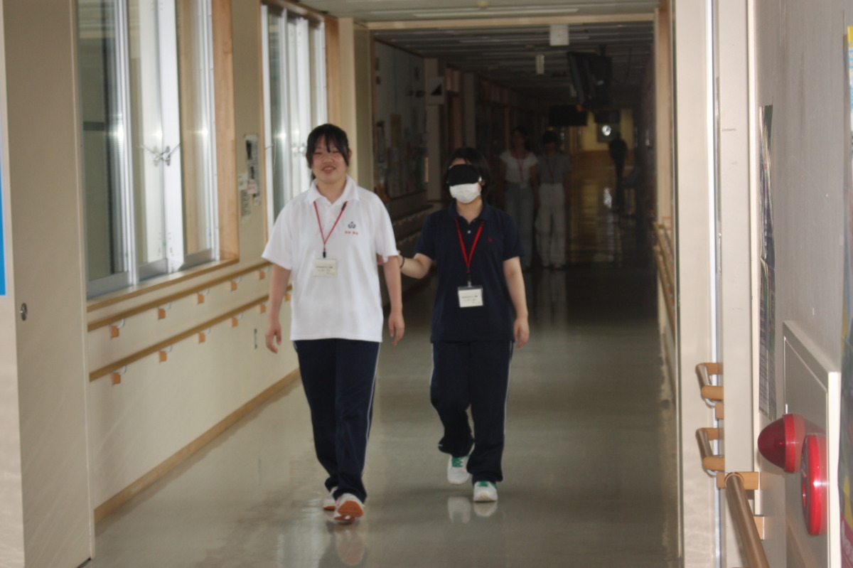 参加者が、アイマスクをした参加者を手引きしながら廊下の奥から歩いてくる様子。