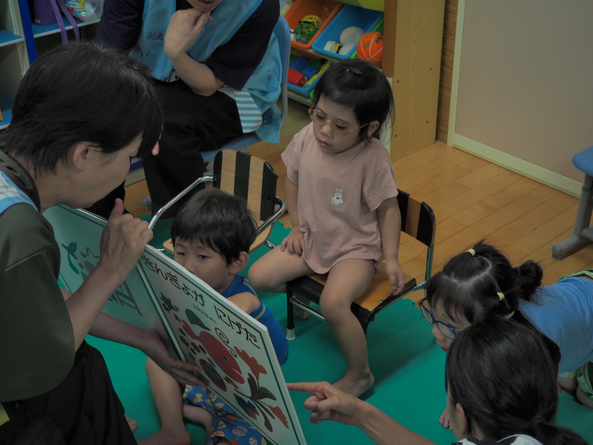 教員が開いている「きんぎょが にげた」の大型絵本を、夢中で覗き込んでいる幼児3名
