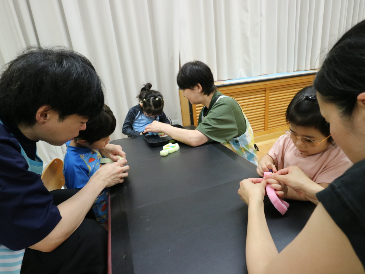 机の3辺に、それぞれ幼児と教員が1名ずつ位置し、各自スポンジの魚を作っている様子。