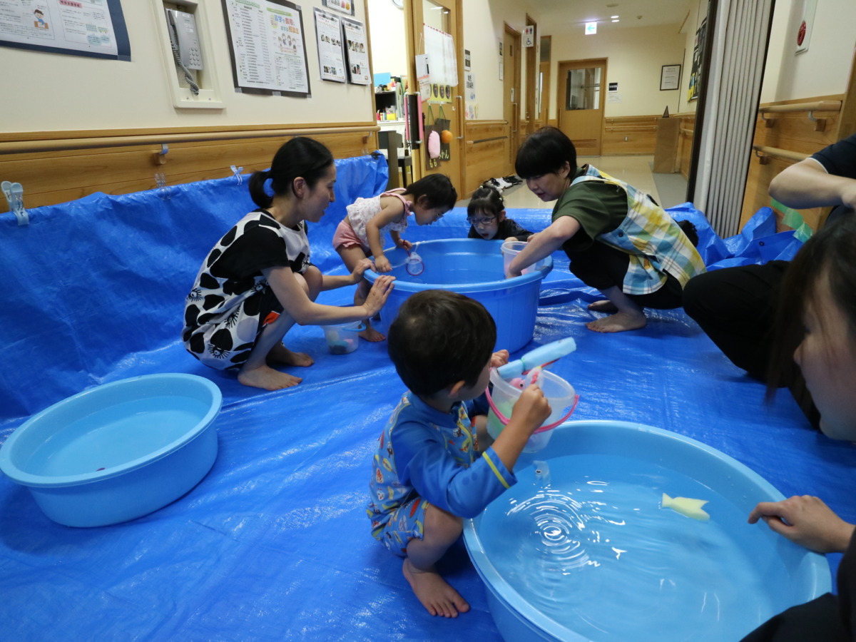 廊下にブルーシートを敷き、青色のたらいの中に張った水に各自スポンジの魚を浮かべている様子。