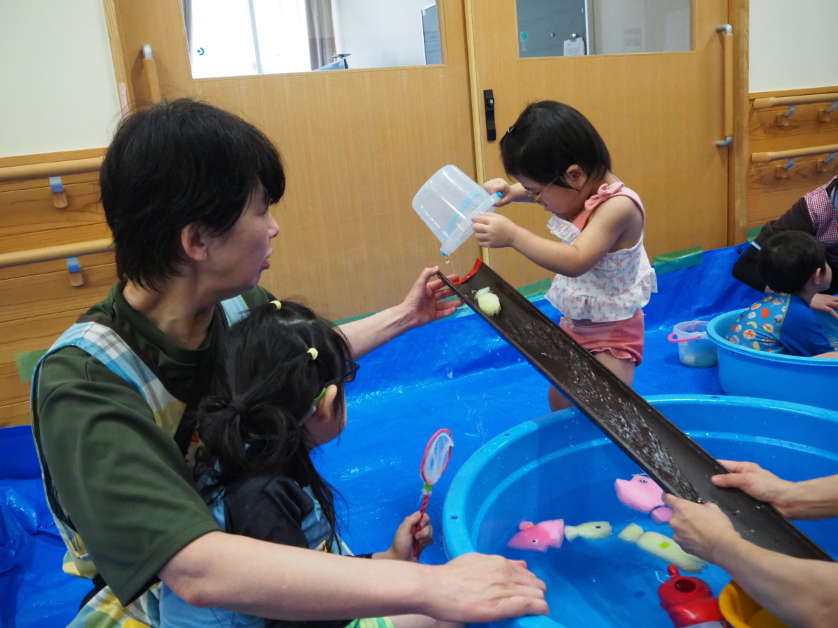 勾配具を教員に支えてもらいながら、自分の魚を滑り台のようにたらいに流す幼児